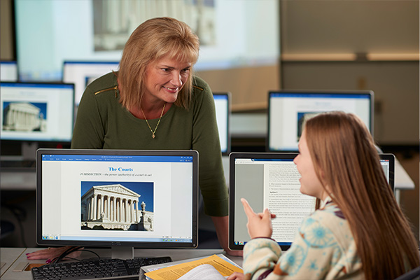 Teacher leans toward student looking at Supreme Court website on computer